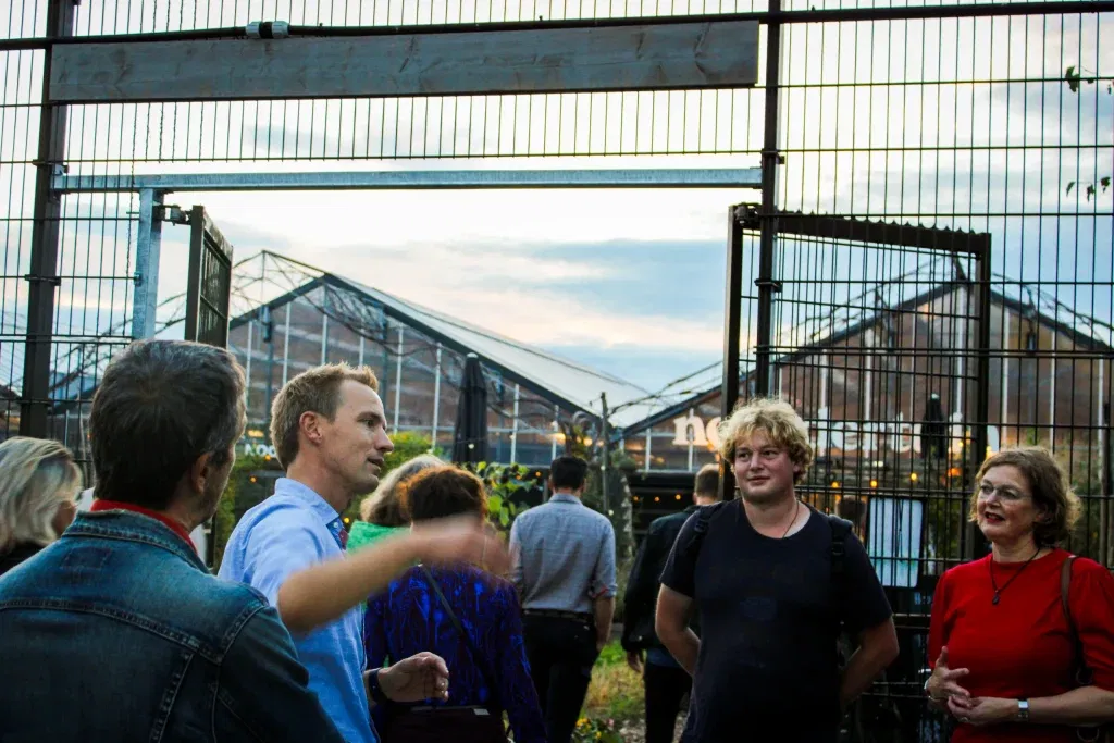 Tijdens een informatieavond krijgen bezoekers een rondleiding over het terrein van Steck. In de voorgrond is een groepje mensen te zien, in de achtergrond de kassen van Steck en tuincafé Noordertuin