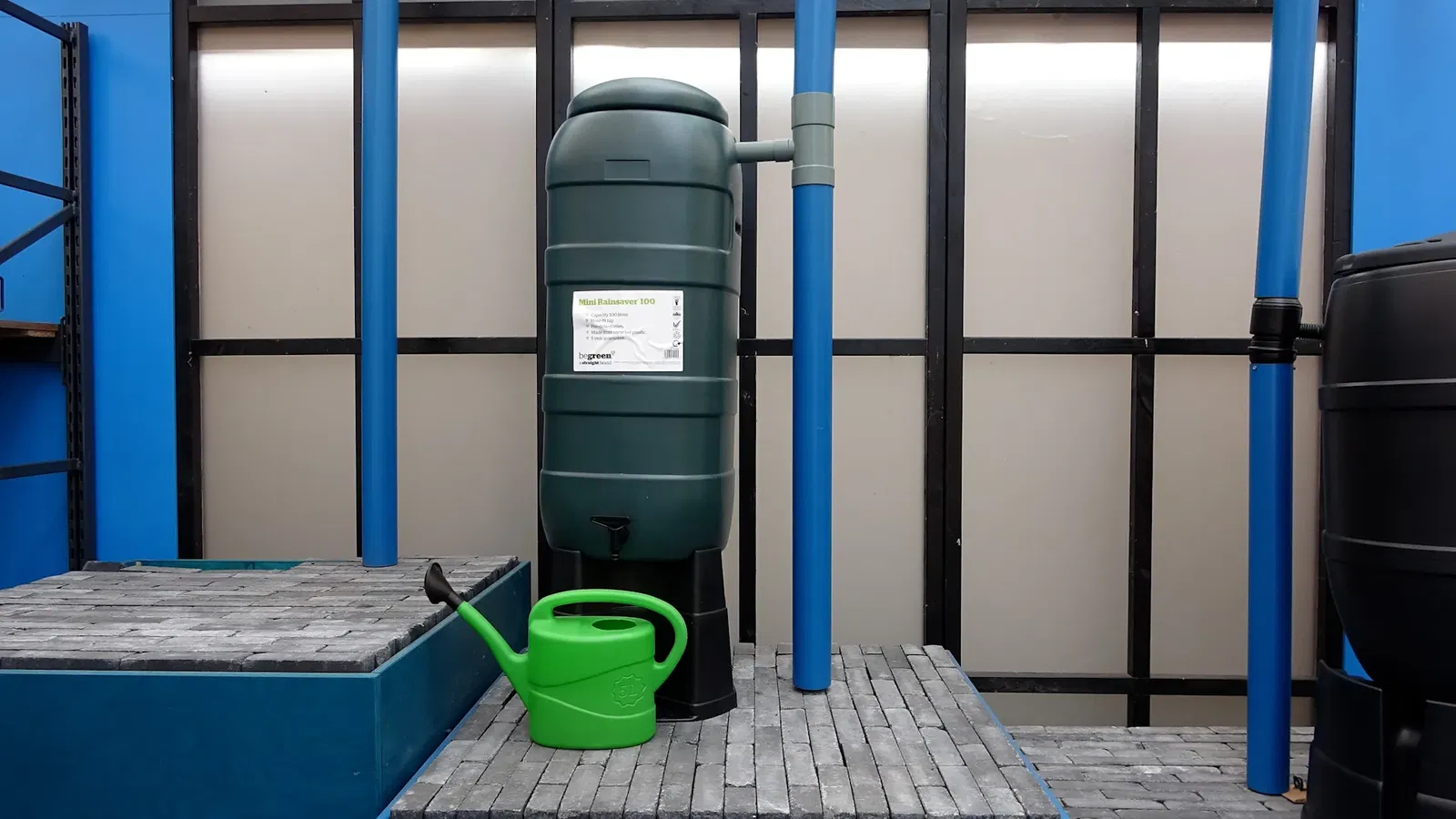 Een regenton in tuincentrum Steck in Utrecht Overvecht, aangesloten op een voorbeeld regenpijp met een gieter ernaast