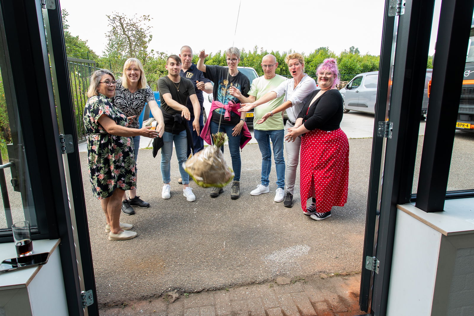 Een groep vrolijke mensen staat buiten voor de ingang van Steck, terwijl ze een bos bloemen in de lucht gooien. Ze zijn duidelijk enthousiast en vieren een speciaal moment.