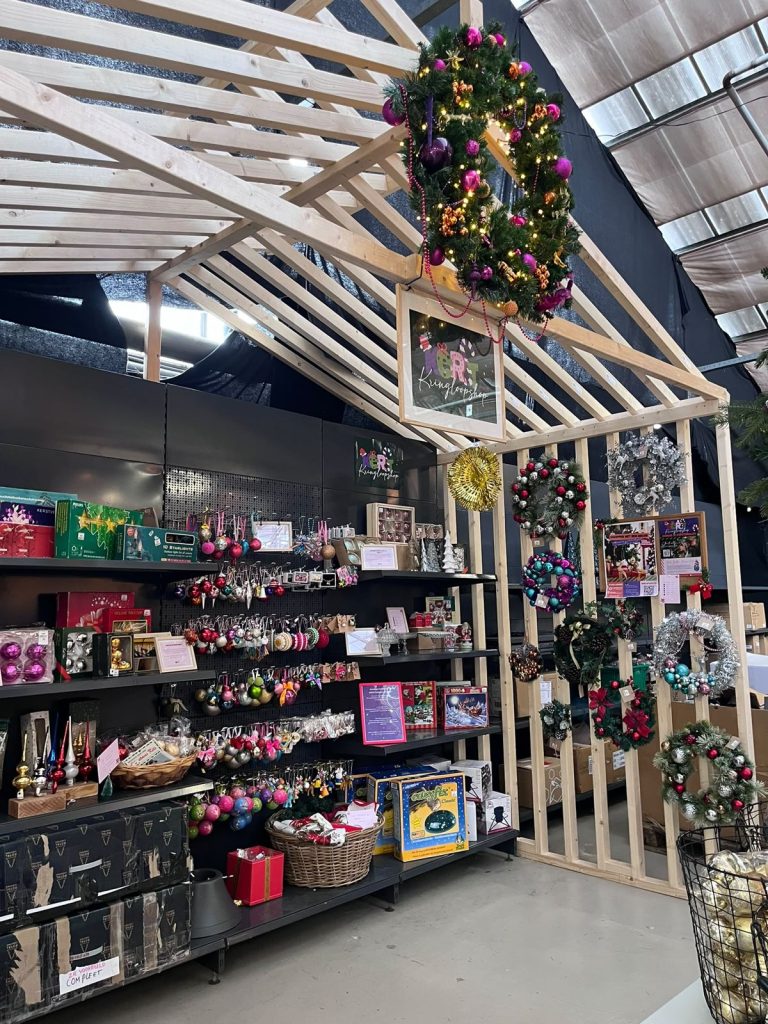 De Kerst Kringloopshop binnen bij Steck: schappen vol tweedehands kerstballen en een wand met kransen