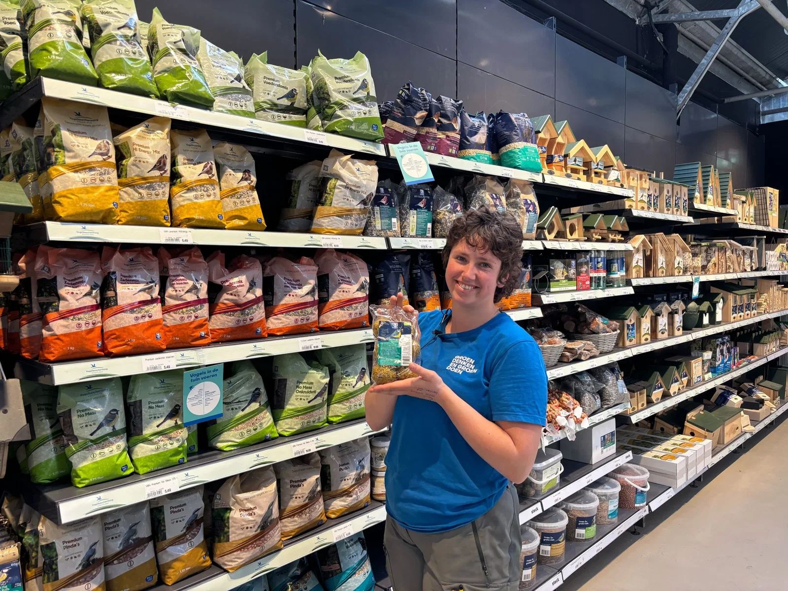 Medewerker van Steck met vogelvoer voor het schap met vogelvoer en nestkastjes